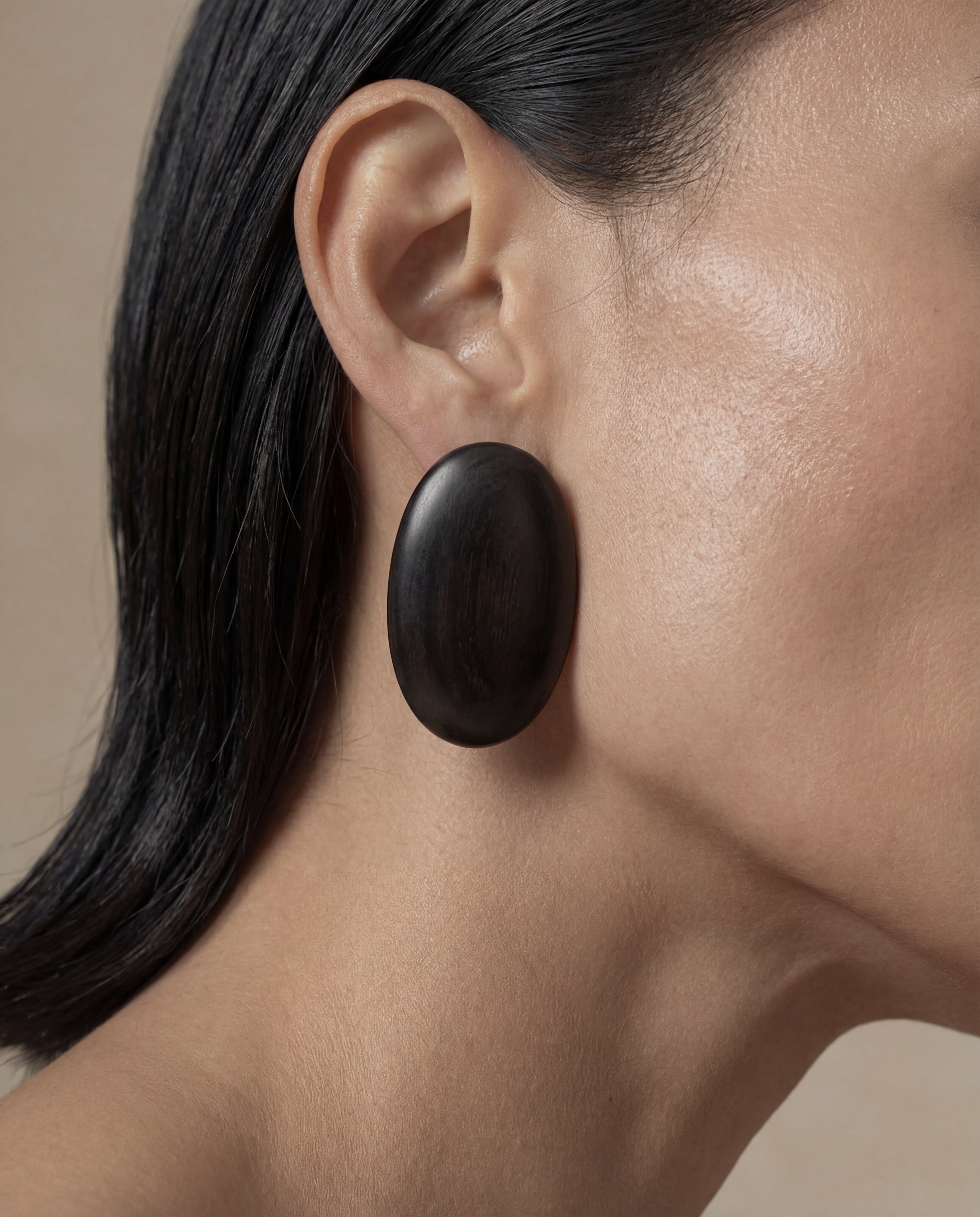 Model wearing a large, oval shaped black wooden earring.